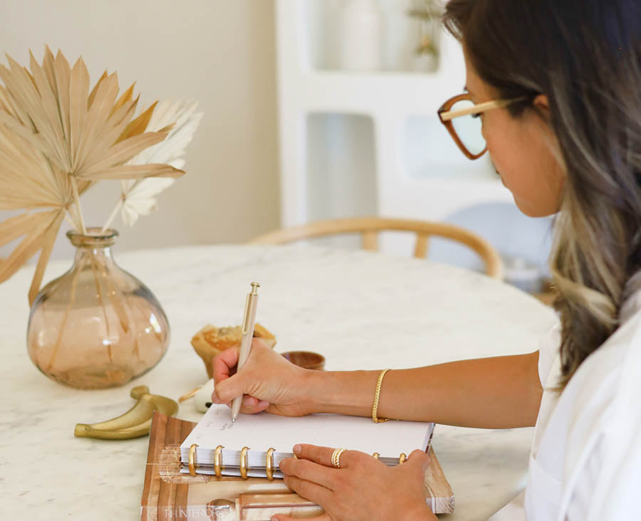 Woman writing in an InkWELL Press planner while sitting at a table.