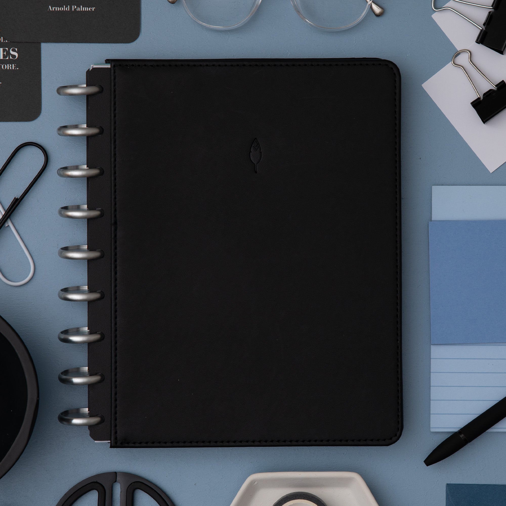 black faux leather cover with silver disc on this inkwell planner surrounded by office supplies