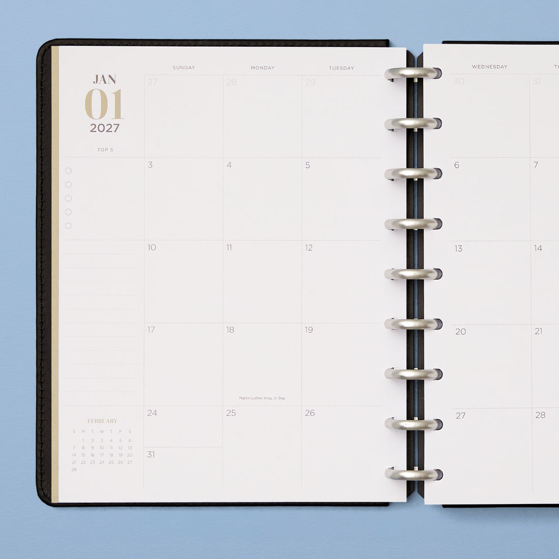 An open disc-bound planner showing a monthly calendar spread with lined notes section and reference calendar, and bullet points